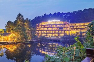 Un hotel con un letrero grande, varios pisos y un reflejo en el agua.