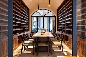 Un comedor con una mesa larga, numerosas sillas y estanterías llenas de vasos a ambos lados.