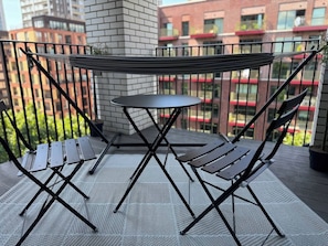 A balcony with a table and chairs, a view of buildings, and a brick wall. - City Base: 2 Beds, 2 Baths, Balcony, Lift (Greater London)