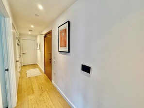 A hallway with wooden flooring, white walls, and a framed artwork. - City Base: 2 Beds, 2 Baths, Balcony, Lift (Greater London)