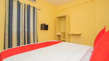 Una habitación de hotel con cama, cortinas, un televisor y una estantería de madera.