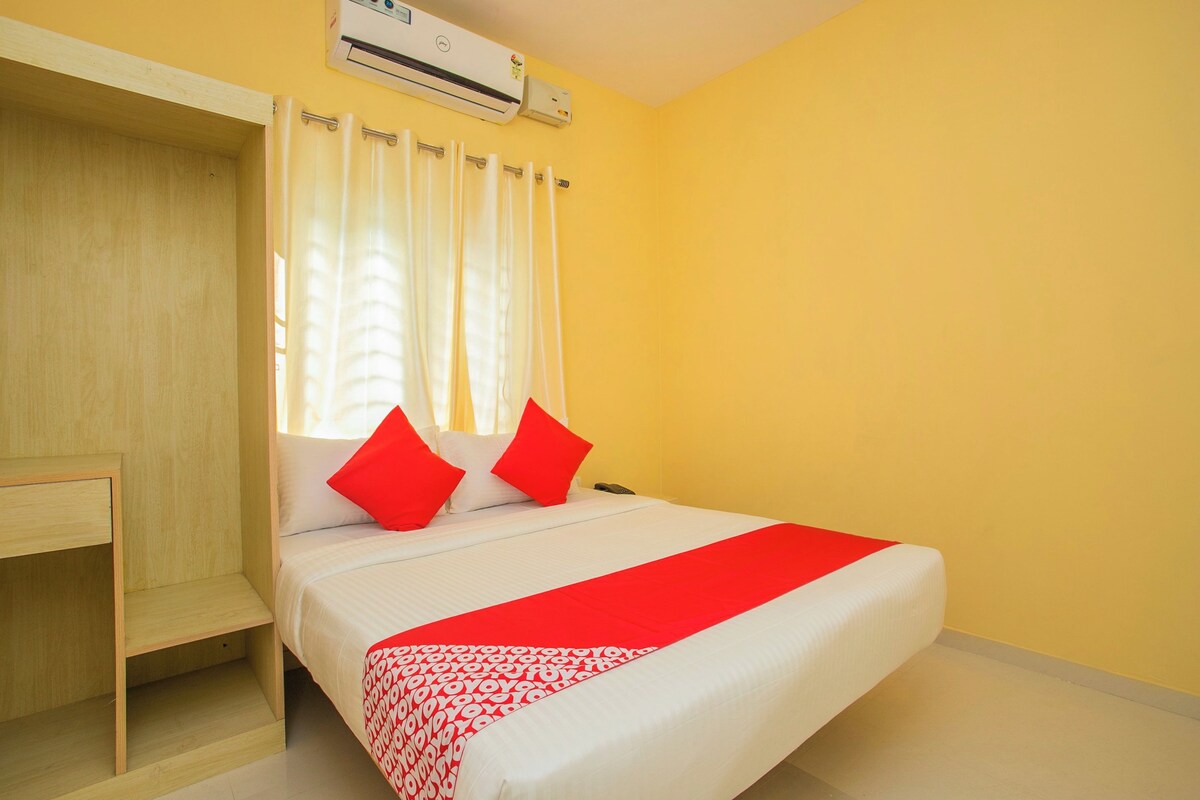 A hotel room with a bed, a desk, and an air conditioning unit.
