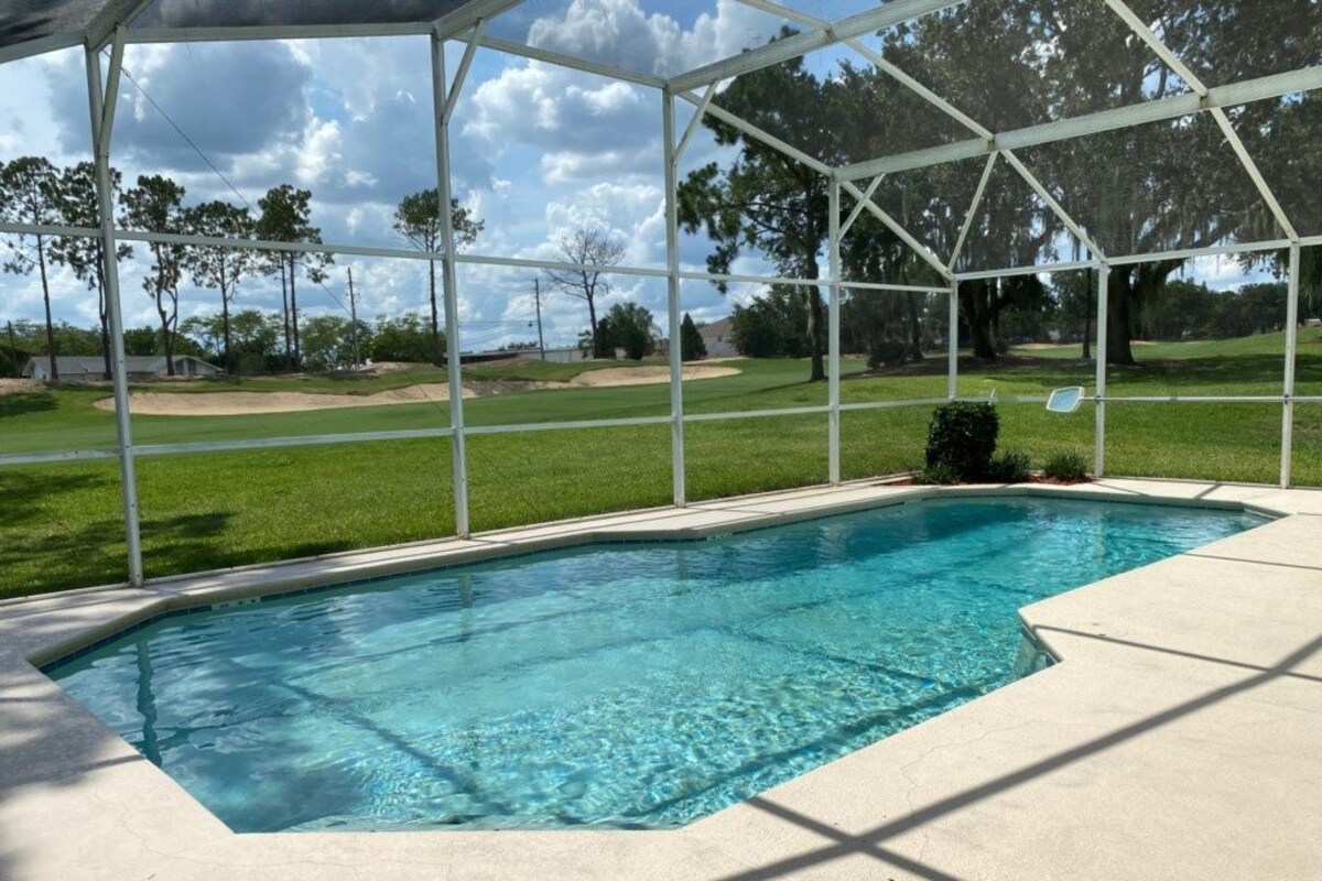 A swimming pool with a covered area, surrounded by a grassy lawn and trees.