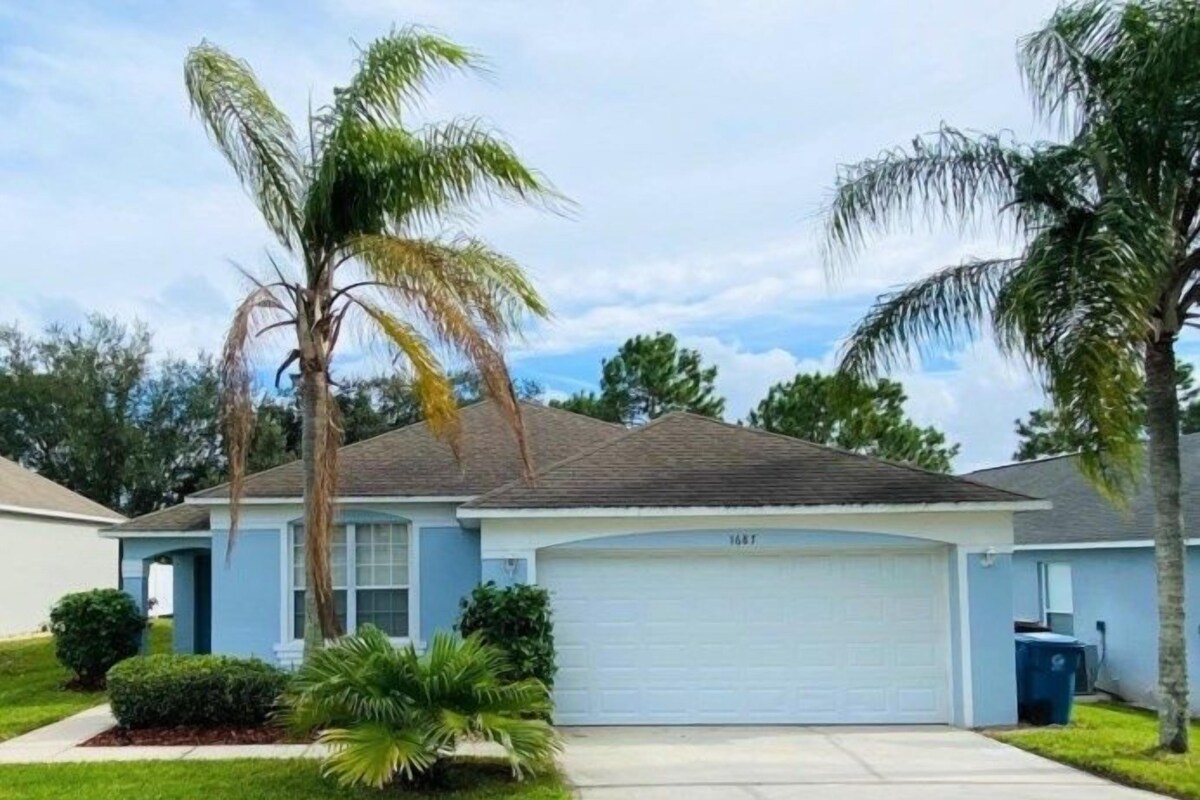 A single-story house with a garage, a lawn, and palm trees.