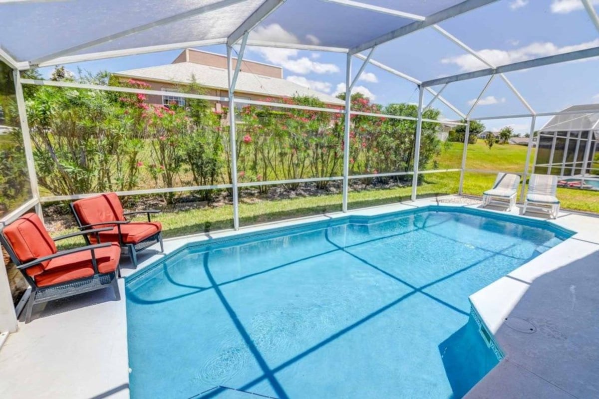 A covered swimming pool with a clear view of the surrounding landscape, including a house and greenery.