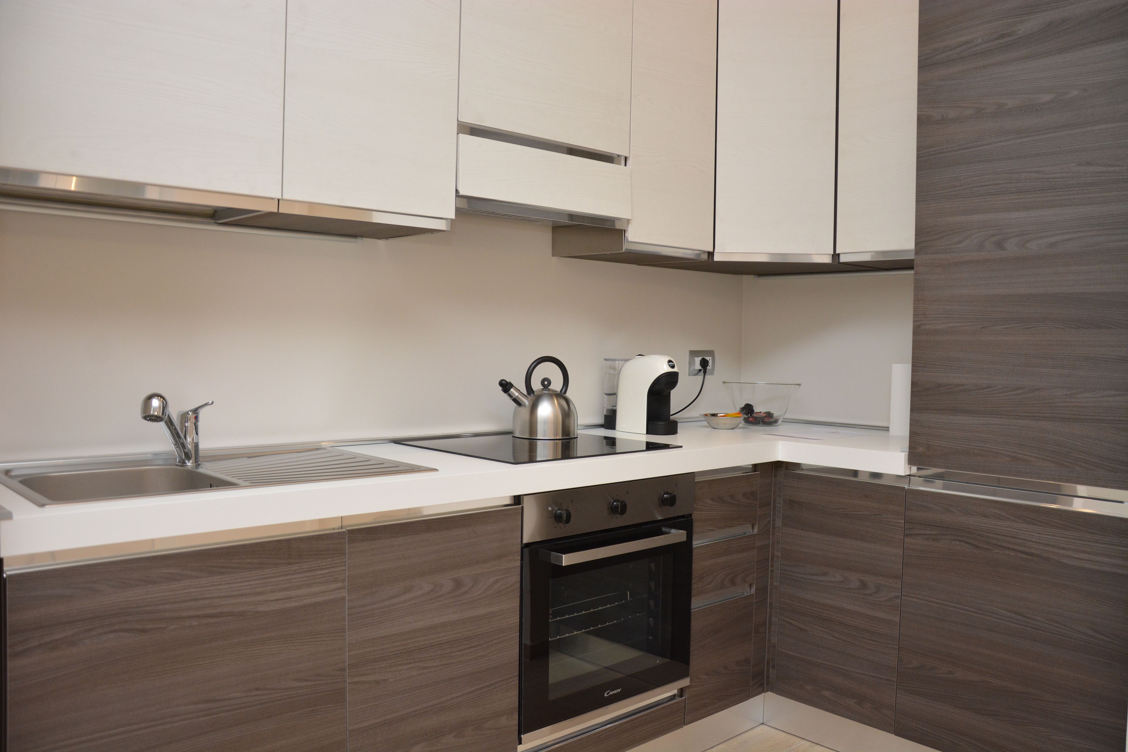 Una cocina moderna con un lavamanos de acero inoxidable, una tetera, una cafetera y un horno empotrado.