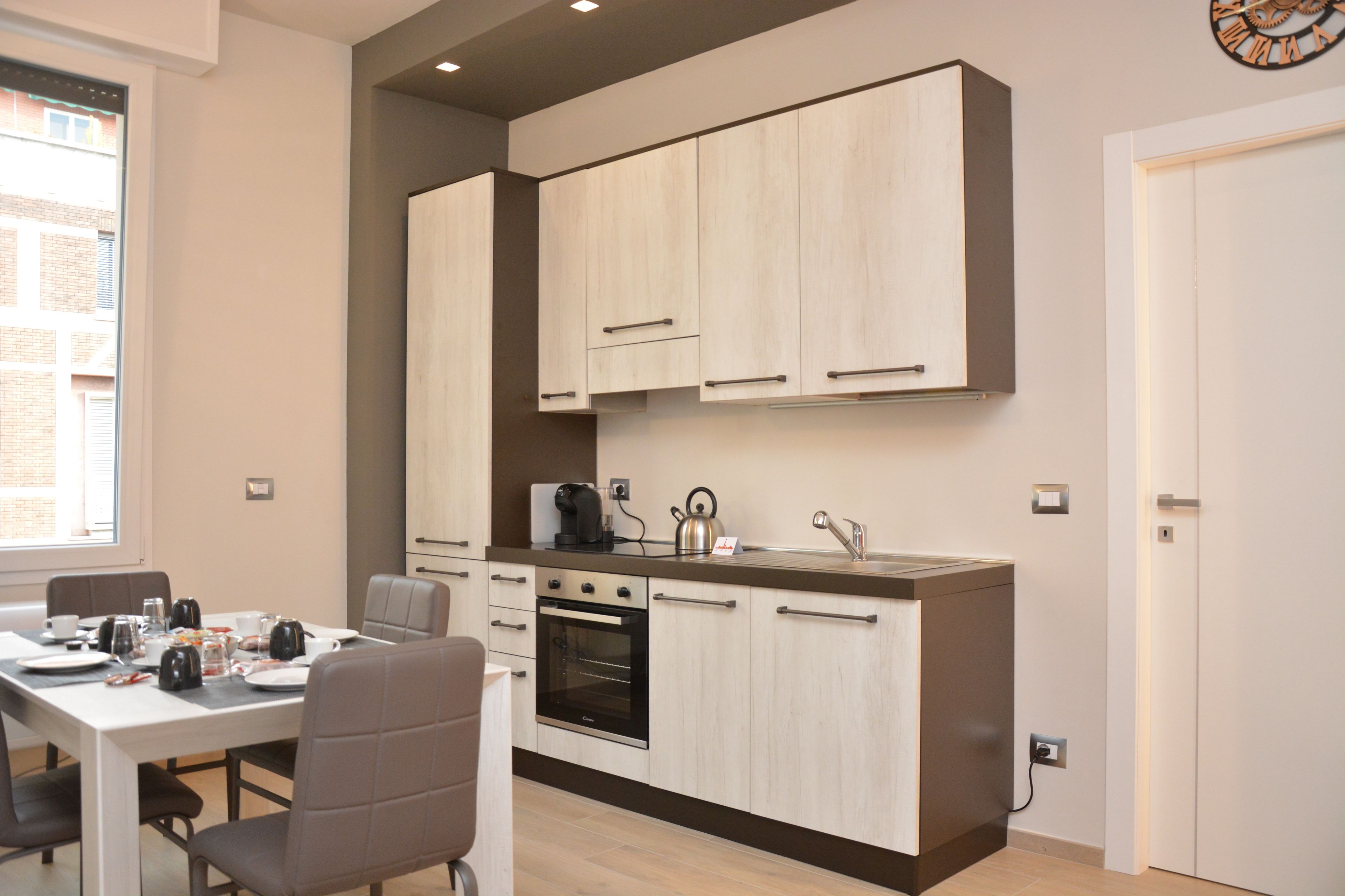 A compact kitchen with modern appliances, a dining area with a table and chairs, and a view of the outside through a window.