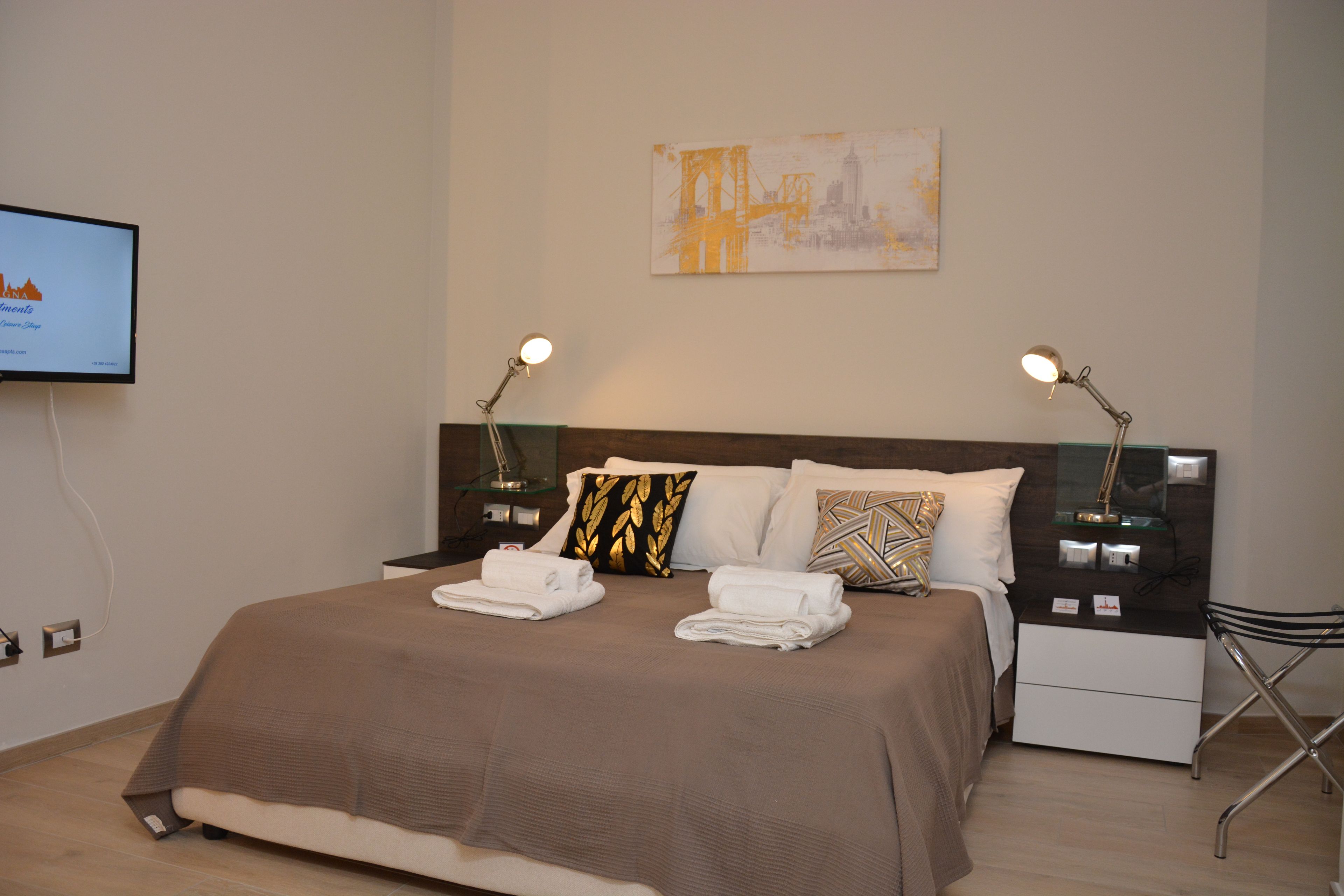 Ein Hotelzimmer mit einem Bett, zwei Nachttischen, einem Flachbildfernseher und einem Bild an der Wand.