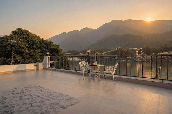 A terrace with a view of a river and mountains, featuring a table and chairs.