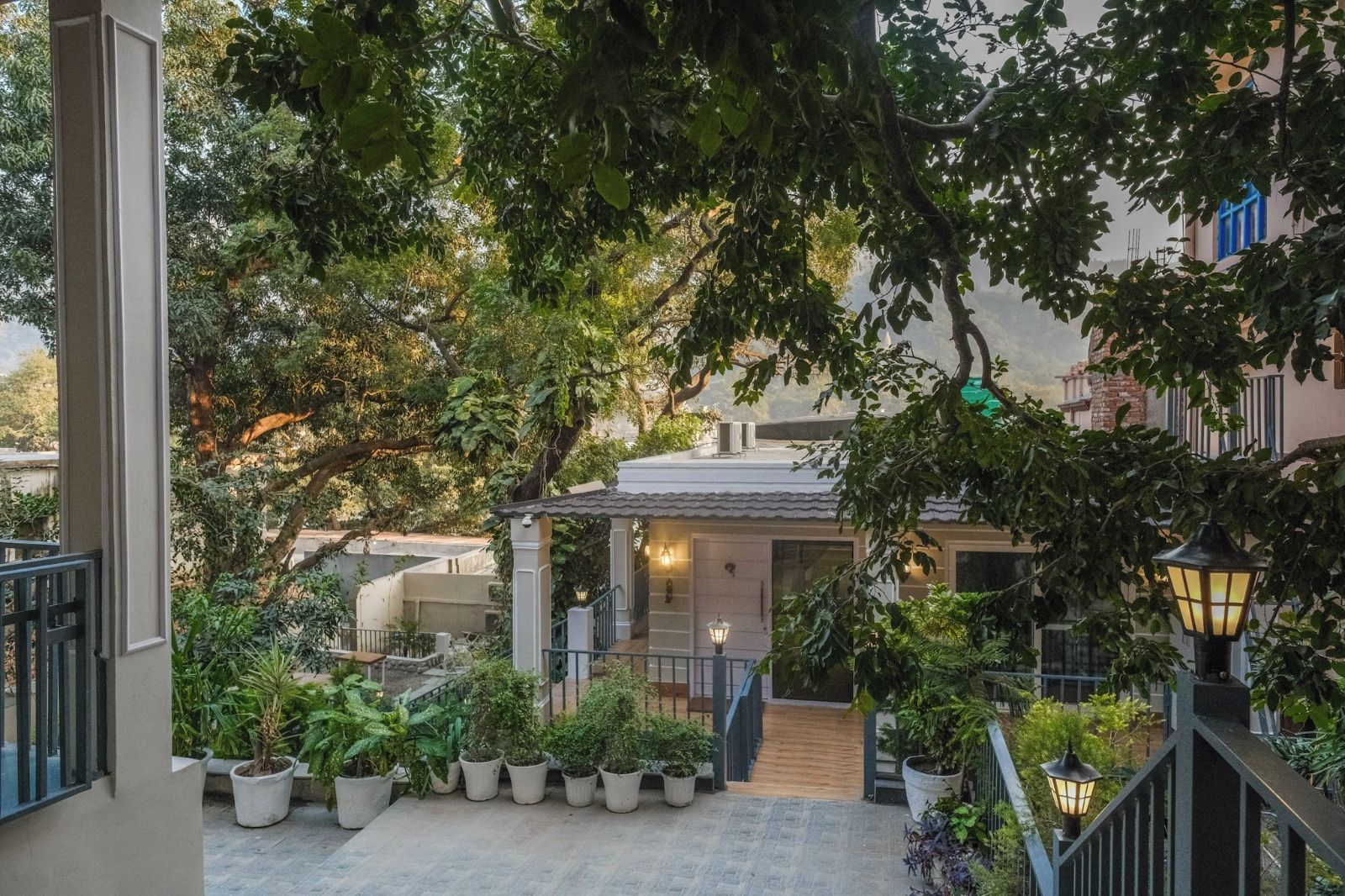 Un patio con una escalera que lleva a un edificio, rodeado de plantas en macetas y árboles.