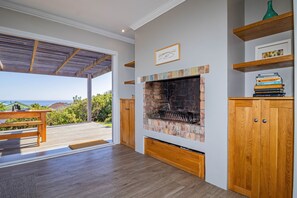A modern living room with a fireplace, wooden furniture, and a view of the outdoors. - Cloud 7 | Peaceful | Mountain & sea views | Onrus (Onrusrivier)