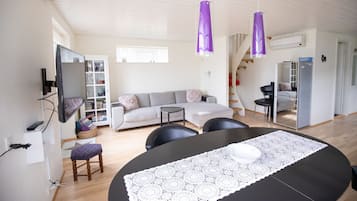 Een moderne woonkamer met een bank, een eettafel met een kantrondom tafelkleed, en paarse hanglampen.