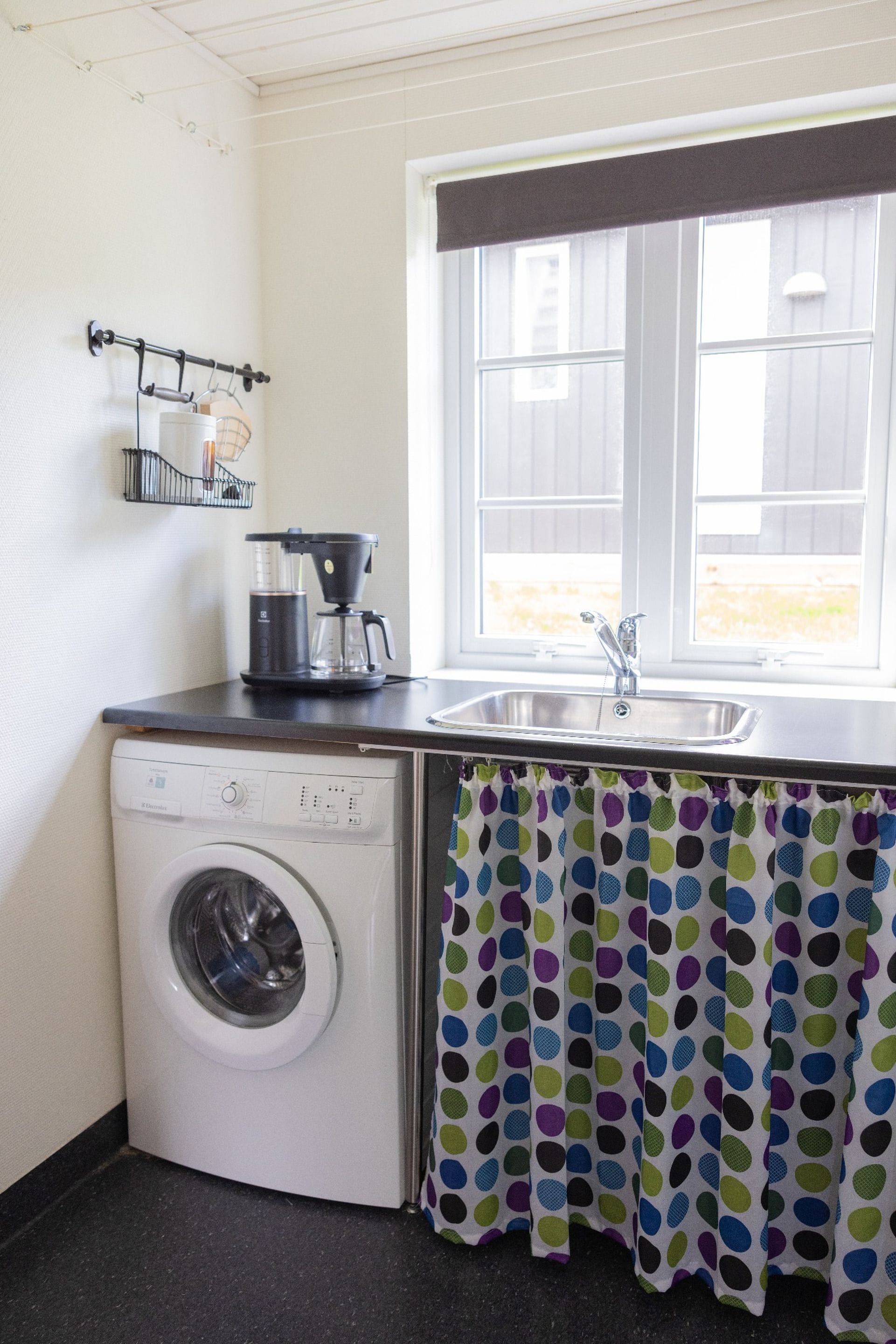 A compact kitchen with a washing machine, a coffee maker, and a window with a view.