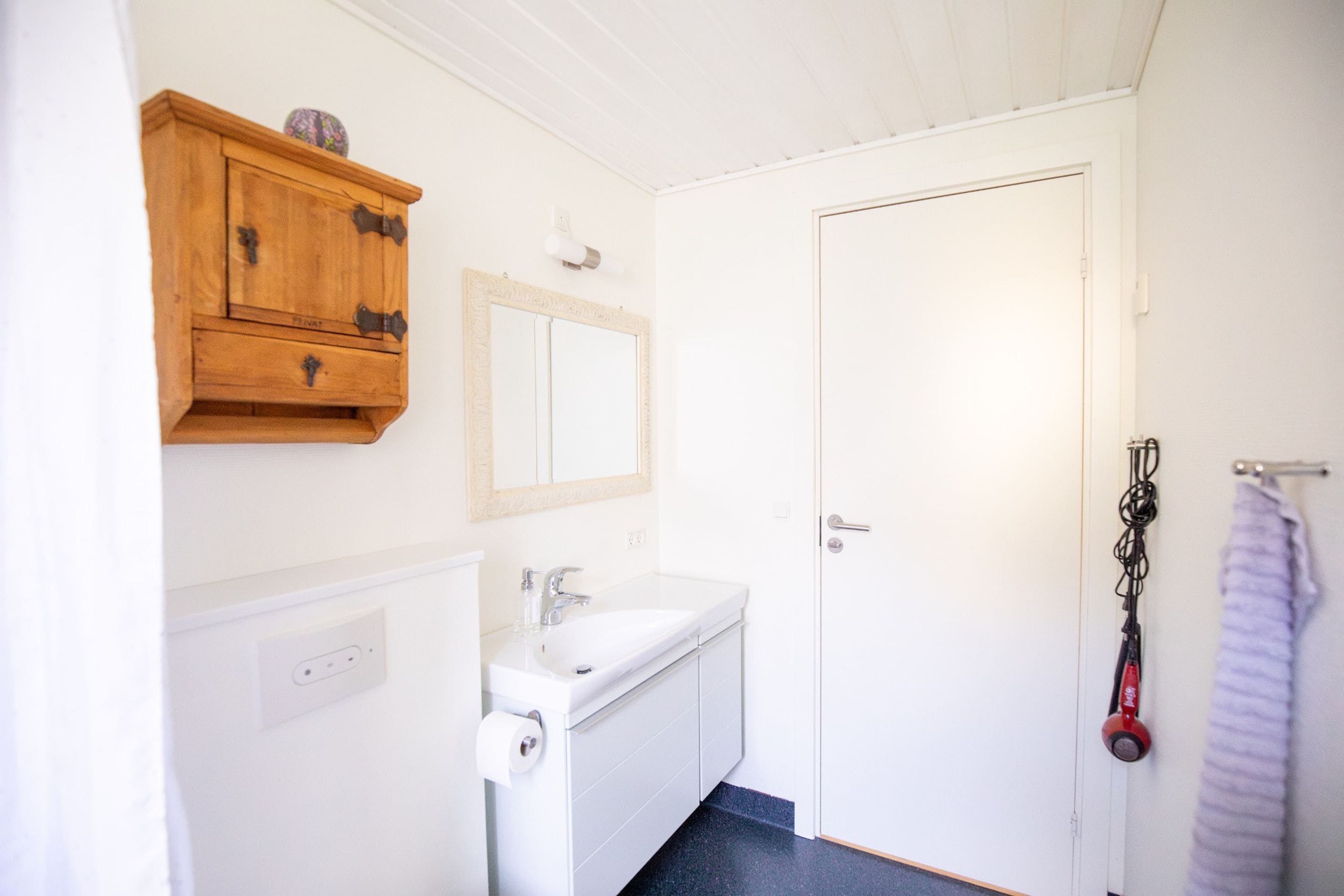 Un baño con un lavamanos blanco, un armario de madera, un espejo y una puerta.