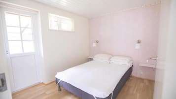 A bedroom with a single bed, a door, a window, and a wall-mounted light fixture.