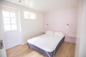 Une chambre avec un lit simple, une porte, une fenêtre et un luminaire fixé au mur.