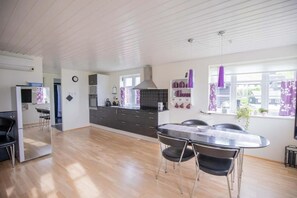 A modern kitchen with a dining area, wooden floors, and a view of the outside. - Eystan Gard 5H (Gjógv)