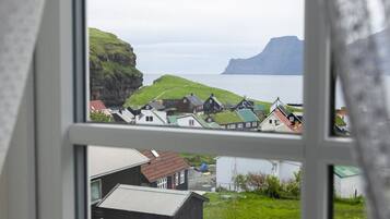 En utsikt från ett fönster över en kustby med hus, gräsbevuxna fält och en klippa.