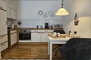 Eine moderne Küche mit weißen Schränken, einer Holzausziehtafel, einer Mikrowelle, einer Kaffeemaschine und einem Essbereich mit Tisch und Stühlen.