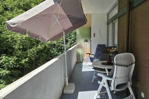 Ein Balkon mit Tisch, Stühlen, einer Topfpflanze und einem Sonnenschirm.