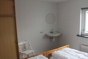 A small, simple room with a bed, a chair, a wooden wardrobe, a wall-mounted sink, and a window. - Bungalow with 2 bedrooms (Callantsoog)