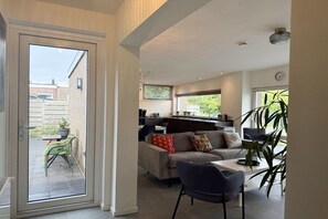 A modern living room with a sofa, a dining table, and a chair. There is a sliding glass door leading to an outdoor area with a table and chairs. - Holiday home with 2 bedrooms (Julianadorp)