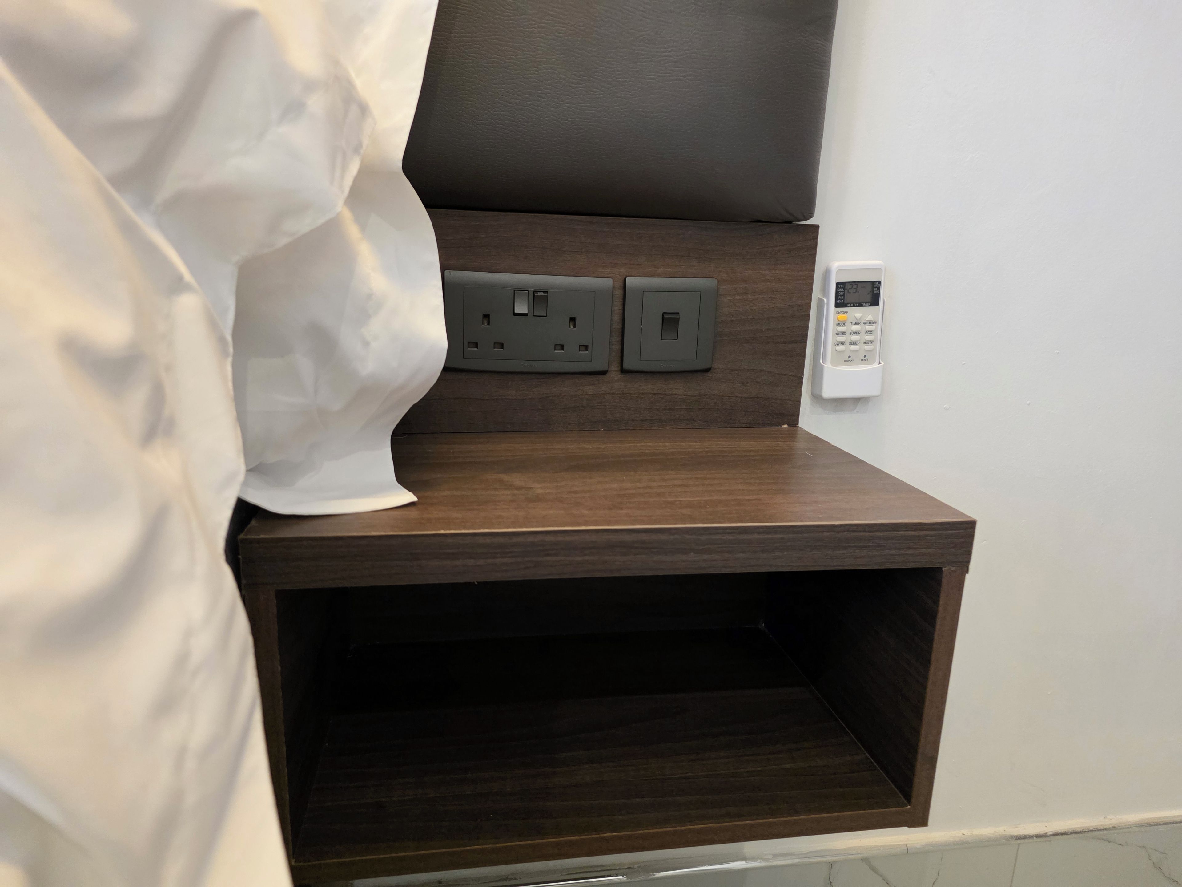 A wooden bedside table with a power outlet and a control panel, likely for a bed or desk lamp.