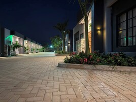 A paved walkway leading to a row of modern buildings with illuminated windows and outdoor lighting.