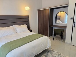 Una habitación de hotel con cama, mesita de noche, una silla verde, armario y espejo.