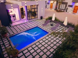 A swimming pool with a tiled deck, lounge chairs, and umbrellas.