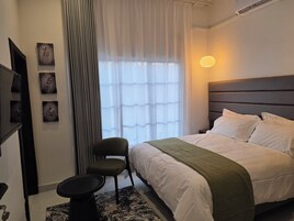 A modern bedroom with a bed, a chair, a small table, and artwork on the wall.