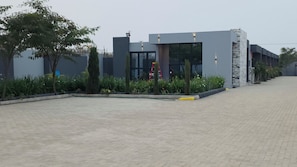 Um edifício moderno com área de entrada pavimentada, uma escada e um jardim bem cuidado.