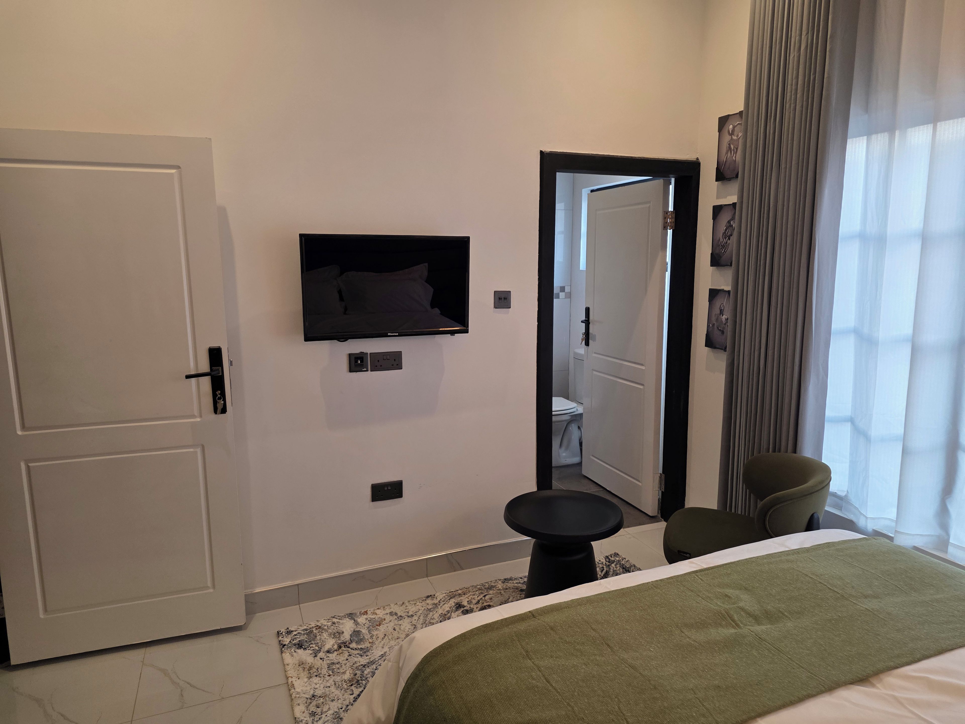 Une chambre d’hôtel avec un lit, une petite table, une chaise, un téléviseur fixé au mur et une porte de salle de bain visible au fond.