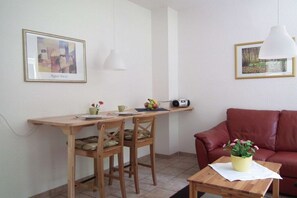 A small, cozy room with a wooden table, two chairs, a red sofa, and a wall-mounted shelf with a framed picture. - Holiday apartment in Ilsenburg with terrace (Ilsenburg)