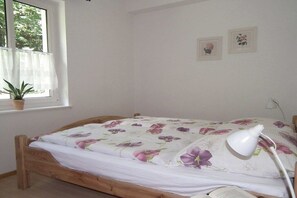 A bedroom with a wooden bed, a window with a plant, and a wall-mounted lamp. - Holiday apartment in Ilsenburg with terrace (Ilsenburg)