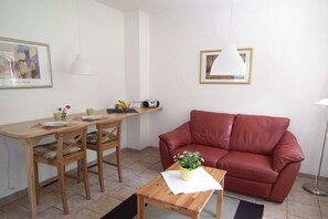 A living room with a red sofa, wooden dining table, chairs, a small table with a plant, and a framed picture on the wall. - Holiday apartment in Ilsenburg with terrace (Ilsenburg)