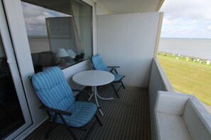Un balcon avec deux chaises et une petite table, une fenêtre avec des rideaux et une vue sur la mer.