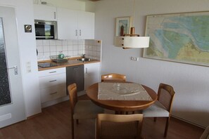 A compact kitchen with white cabinets, a microwave, and a dining area with a table and chairs. - Holiday apartment with 1 bedroom (Cuxhaven)