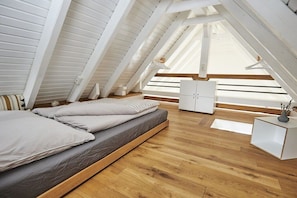 Ein Schlafzimmer mit schrägen Wänden, Holzboden, einem Bett mit grauer Bettwäsche, einem weißen Nachttisch und einem weißen Kleiderschrank.