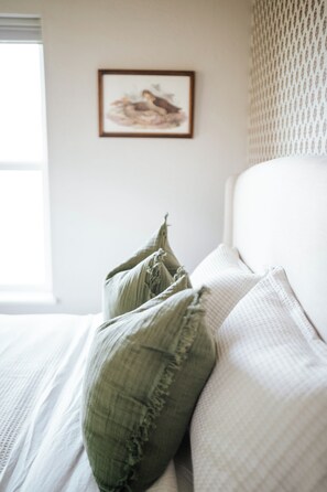 Een opgemaakt bed met groene kussens en een lijst met een afbeelding aan de muur.