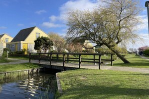 Een woonwijk met een klein bruggetje over een gracht, een pad omzoomd met bomen, en huizen met schuine daken.