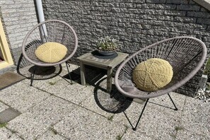 Two wicker chairs with round cushions, a small wooden table, and a potted plant between them. - Holiday home with 1 bedroom (Julianadorp)