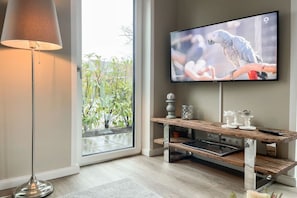 A modern living room with a flat-screen TV mounted on the wall, a floor lamp, and a wooden coffee table with decorative items. - Holiday apartment with 2 bedrooms (Scharbeutz)