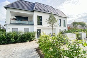 A two-story residential building with a balcony, a driveway, and surrounding greenery. - Holiday apartment with 2 bedrooms (Scharbeutz)
