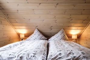 Ein Zimmer mit schrägen Wänden, zwei Betten mit gemusterten Bettdecken und Wandlampen.