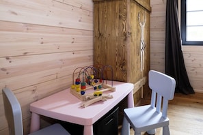 Ein Zimmer mit Holzwänden, einem rosafarbenen Tisch mit einer Spielzeug-Eisenbahnstrecke und einem weißen Stuhl.