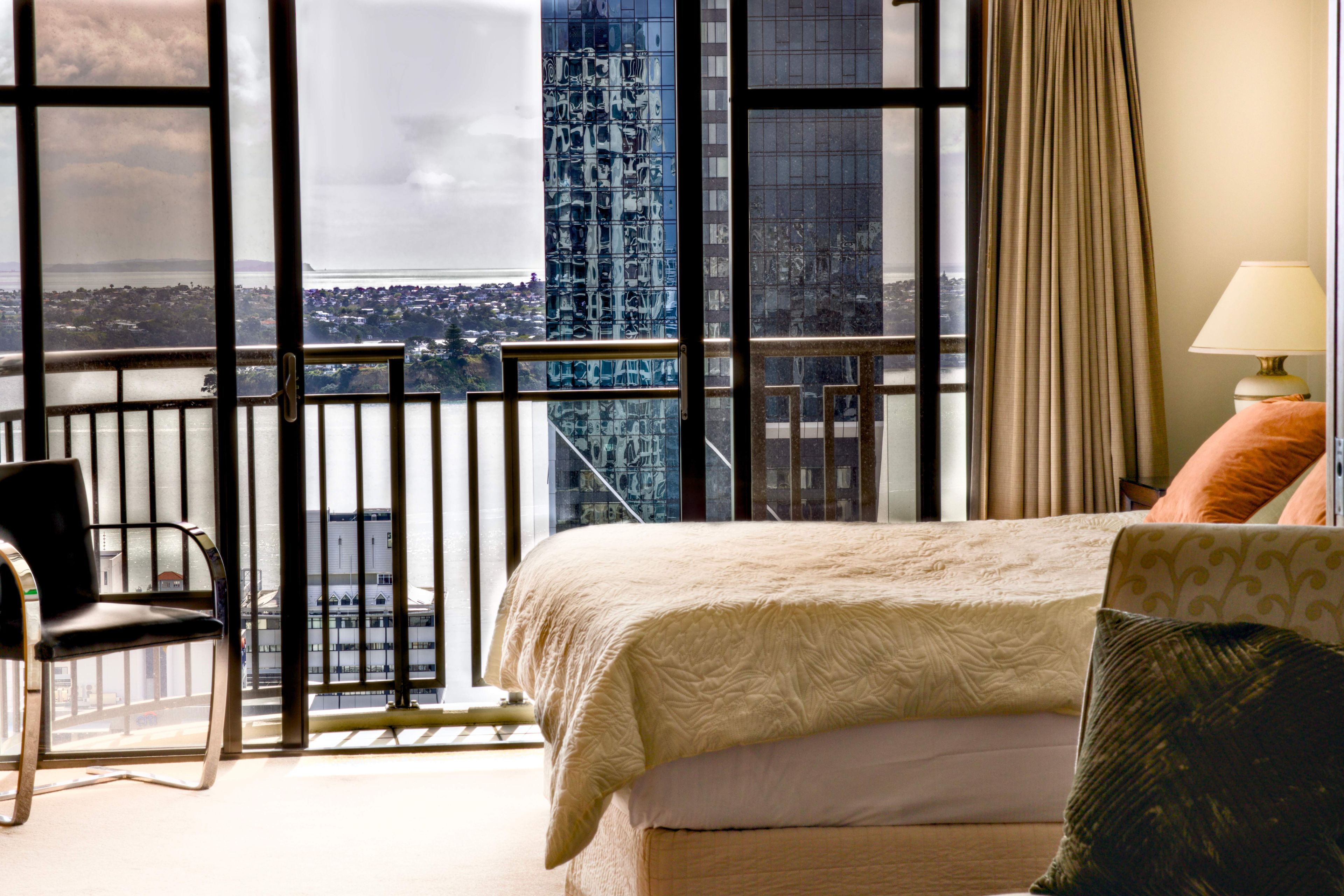 A hotel room with a bed, a chair, a window with a view of a cityscape, and a curtain.