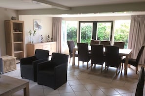 A dining area with a table and chairs, a sofa, a cabinet, and a window with a view of greenery. - Holiday home with 2 bedrooms (Julianadorp aan Zee)