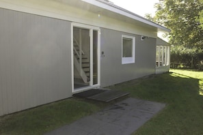 A single-story building with a sliding glass door entrance, a small porch, and a visible staircase leading to an upper level. - Holiday home with 2 bedrooms (Julianadorp aan Zee)