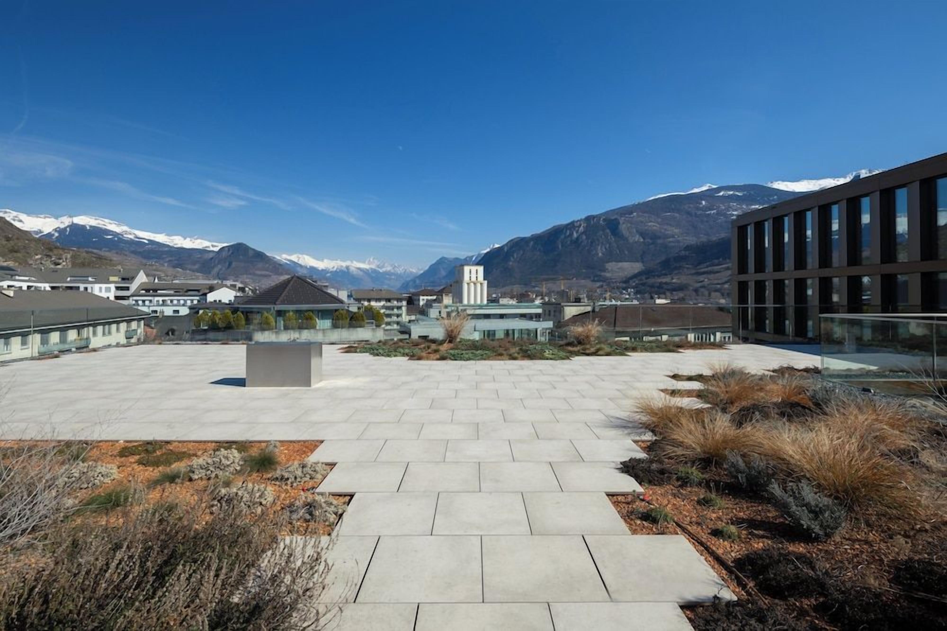A courtyard with a paved walkway, a central seating area, and a mountain backdrop.